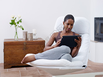 妇女在家里使用平板电脑沙发女性客厅电子邮件黑发背心药片扶手椅享受中年人图片