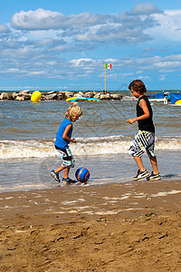在海滩上踢足球足球青少年男生兄弟男孩们乐趣跑步荒地运动娱乐图片