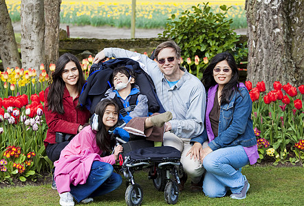 有残疾男孩的家庭在郁金花园中脑瘫轮椅花朵母亲麻痹郁金香混血儿植物群孩子们季节图片