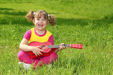 小女孩坐在草地上弹吉他图片