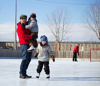 在滑冰场快乐的一家人滑冰爸爸女性兄弟曲棍球男生女孩孩子们溜冰场父母图片
