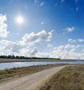 山边有阴云的太阳 在农村道路和附近河流的云上图片