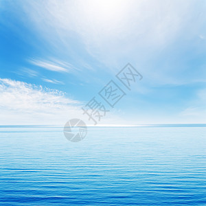 蓝海和有太阳的阴云天空上的光波图片