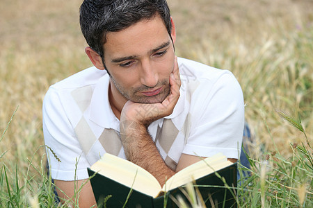 年轻人躺在草地上 阅读一本书图片