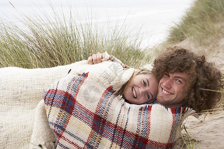 在沙堆中坐着的青少年夫妇合议席男人海滨男性亲热说谎毯子沙丘衣服微笑长发图片