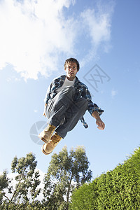 中空中抓获的年轻人在山坡线上跳跃花园休闲服装飞跃低角度男性蹦床精力活力图片