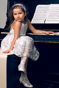 穿着漂亮裙子的女孩坐在钢琴边上爱好钥匙乐趣白色孩子音乐女儿学习学生喜悦图片