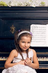 穿着漂亮裙子的女孩坐在钢琴边上学习乐趣孩子音乐喜悦学生爱好白色钥匙女儿图片