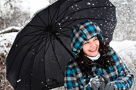 在暴风雪中带着雨伞的年轻女子黑发女性眼睛女士外套天气女孩季节雪花微笑图片