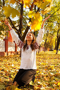 秋天在公园玩叶子的年轻女士图片