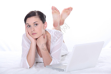年轻妇女躺在笔记本电脑附近的床上图片
