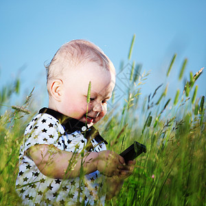 男孩在草地上打来电话孩子微笑蓝色眼睛讲话木头场地婴儿头发技术图片