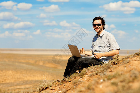 拥有户外笔记本电脑的快乐男人乐趣沙丘商业岩石荒野科学场地天空互联网学习图片