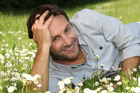 一个微笑的男人躺在花朵的花园里图片