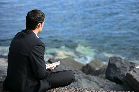 商务人士坐在海边的岩石上图片