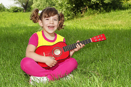小女孩坐在草地上弹吉他唱歌图片
