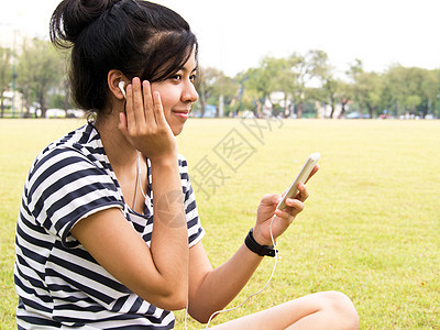 一个有户外耳机的年轻女孩 听音乐手机快乐立体声韵律幸福青年音乐播放器公园音乐享受图片