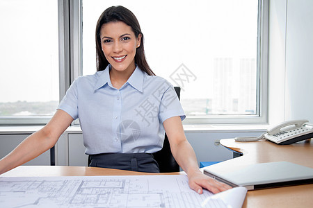 女性建筑师在办公桌上布满蓝图的坐女建筑师图片