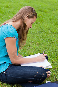 严肃的年轻女孩在她笔记本上写作时坐着图片