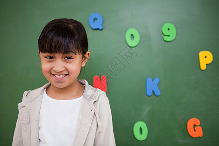带着微笑的女学生 站在黑板前课堂磁铁班级木板孩子知识乐趣数学幼儿园幸福背景