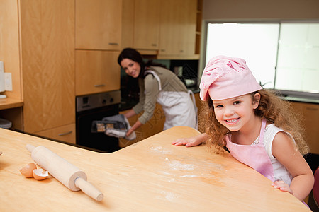 女孩坐在厨房里 而她的母亲把饼干放在T图片