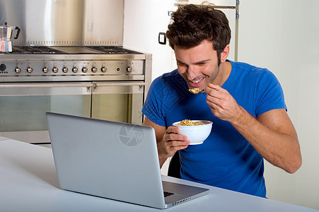 厨房里的男人和笔记本电脑一起吃早餐图片