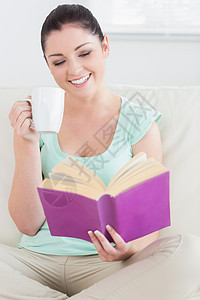 妇女坐在沙发上读书喝酒时坐着图片