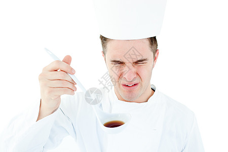 年轻的男厨师在喝汤时用扭曲的面孔图片