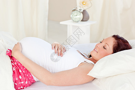 愉快的孕妇睡在卧室的床铺里图片