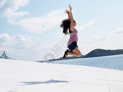 年轻的黑发年轻女性 在屋顶上欢乐的跳跃图片