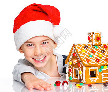 穿着圣诞老人帽子的小男孩和姜饼屋食物假期沙漠蛋糕幸福微笑饼干乐趣糖果传统图片