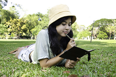女人躺在草地上 在公园里思考闲暇教科书青年幸福女性写作微笑学生女士阅读图片
