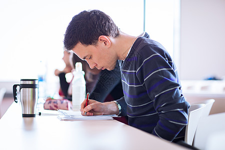 年轻英俊的男大学生坐在满教室的教室里课堂老师团体朋友们笔记本大学白色学习班级女孩图片
