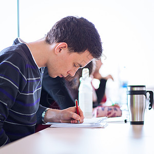 年轻英俊的男大学生坐在满教室的教室里班级水平朋友们青少年白色微笑男人课堂学习校园图片