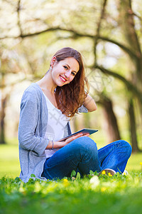 年轻妇女在户外休息时使用平板电脑 同时放松女性校园互联网技术快乐教育季节幸福公园女士图片