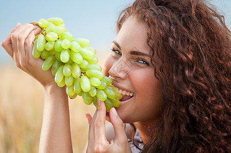 完美的女人在小麦田里吃葡萄自由食物农业微笑国家青少年场地水果卷曲天空图片