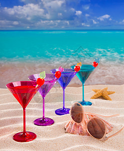 热带沙滩上连着樱桃的彩色鸡尾酒太阳镜海洋柠檬装饰品海星饮料橙子天堂假期紫色图片