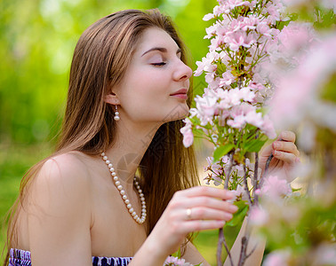 年轻美女闻着粉红樱花花的香味樱花头发公园眼睛裙子魅力女性女孩气味皮肤图片