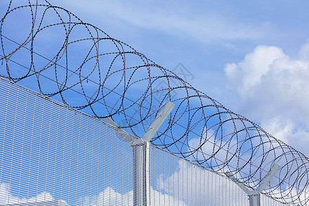 蓝色天空下带刺铁丝网的连链围栏外壳栅栏倒钩防御安全螺旋障碍监狱金属网格图片
