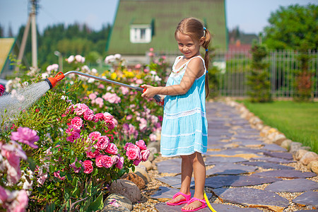 可爱的小女孩在花园里用水管浇花图片