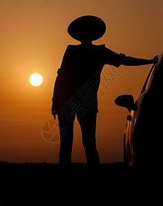 贴着帽子站在汽车旁边的月光妇女女性黑色阴影女孩橙子太阳天空黄色女士图片