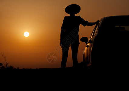 贴着帽子站在汽车旁边的月光妇女黑色黄色女士女孩阴影女性橙子天空太阳图片