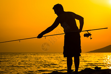 富彩的日落时 渔夫在海滩上的轮廓闲暇钓鱼男人悬崖支撑海岸橙子地平线爱好晴天图片