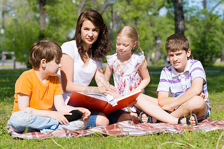 教师读书给夏季公园的孩子看书孩子们男孩们学习说谎阅读女孩微笑教育乐趣快乐图片