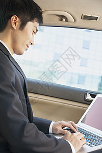 在笔记本电脑上打字汽车后座的商务人士图片