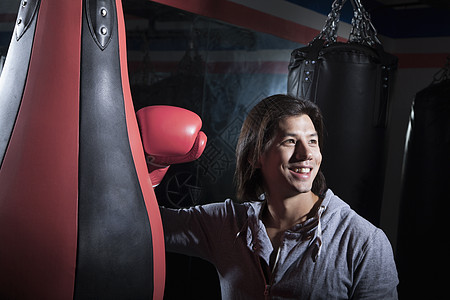 在拳击体育馆时微笑的年轻男子的肖像 仰赖拳打袋图片