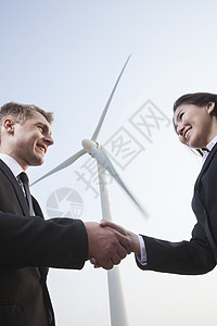 两个微笑着的年轻商务人士 在风力涡轮机前握手图片