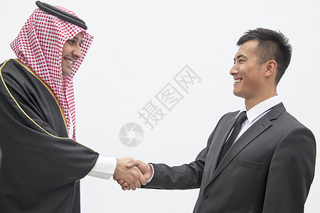 以传统阿拉伯服装为主的微笑商务人士和年轻人握手 拍制工作室拍摄图片