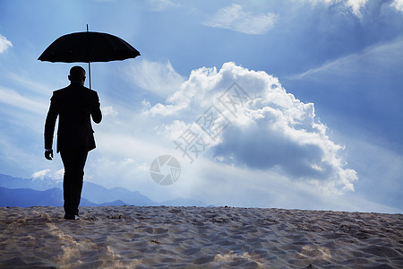 商务人士拿着雨伞 在沙漠中带着梦幻般的云朵走在沙漠中央 然后离开图片