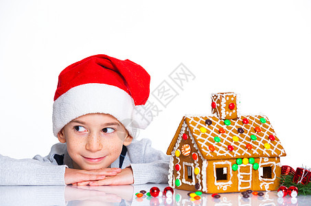 穿着圣诞老人帽子的小男孩和姜饼屋幸福乐趣饼干微笑房子假期孩子沙漠庆典蛋糕图片